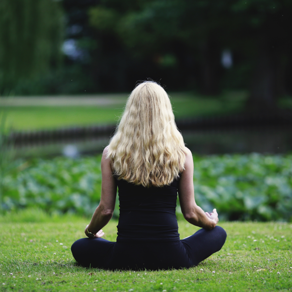 Woman meditating in a peaceful pose on the grass. One Word Mindfulness Meditation