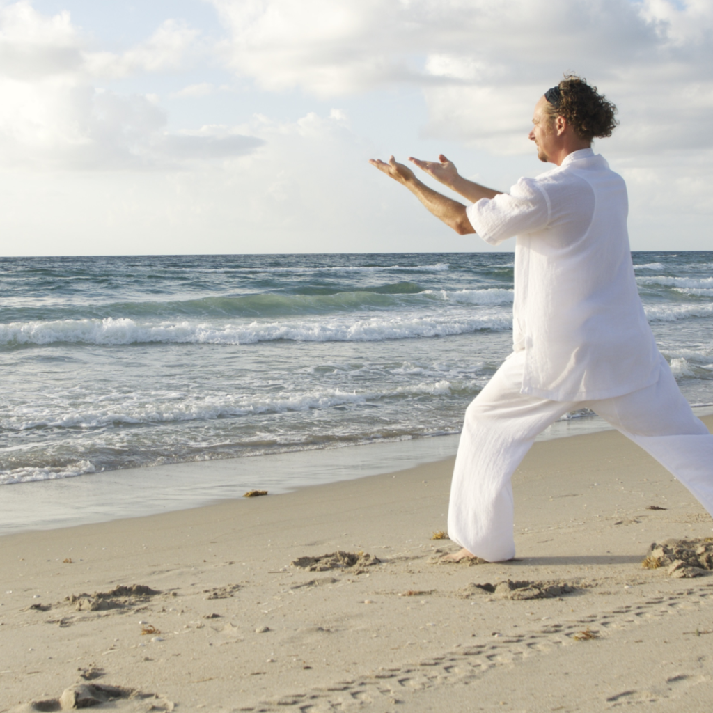 Man in white clothing doing qigong on the beach in the sun for the benefits of qigong
