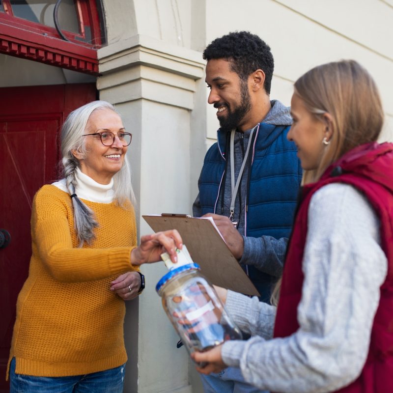 young-door-to-door-fundraisers-talking-to-senior-woman-and-collecting-money-for-charity-in-street.jpg